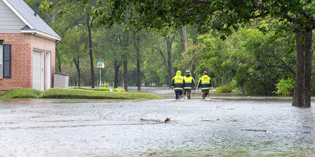 three people in reflective coats walking down a flood street with a house on their left