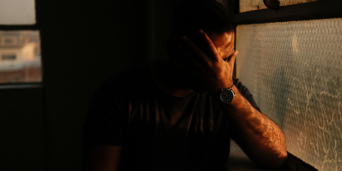 Man in the shadows near a window with his head in his hand