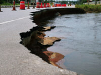 Collapsed road and traffic cones on left with water on right