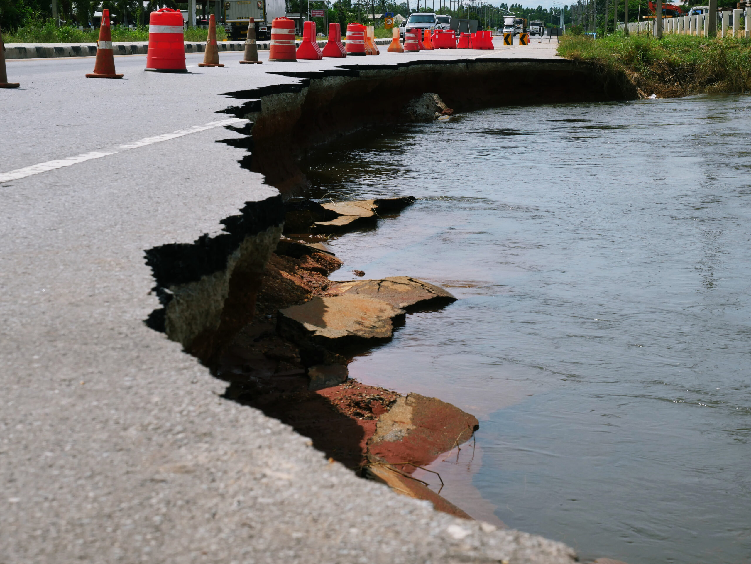 Collapsed road and traffic cones on left with water on right