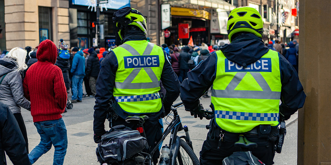 A back view of police officers on bicycles watching a large group of people in a town center