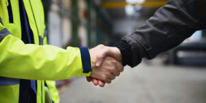 Close up of hands shaking, one with yellow safety jacket and other with black tactical jacket