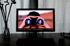 Desk with a vase next to a TV, with a picture of a man holding binoculars with the Facebook symbol on each lens