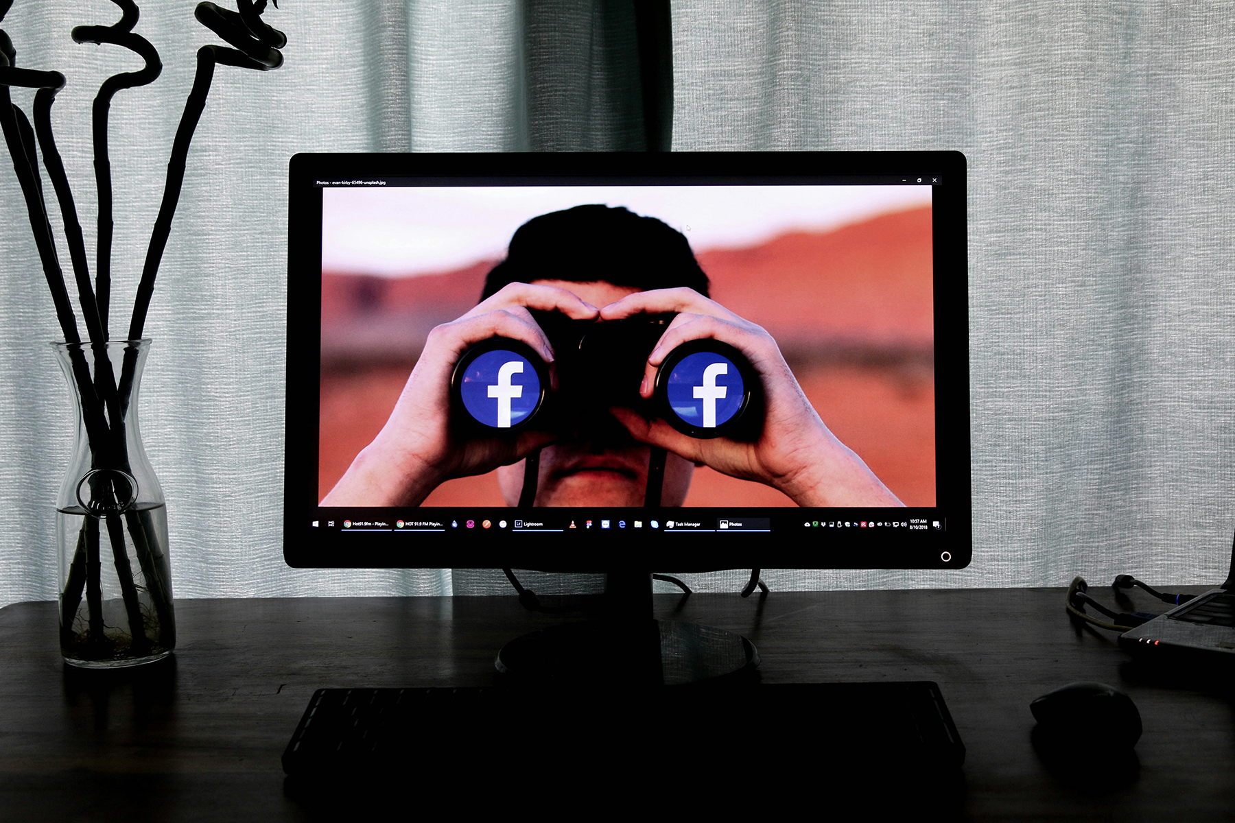 Desk with a vase next to a TV, with a picture of a man holding binoculars with the Facebook symbol on each lens