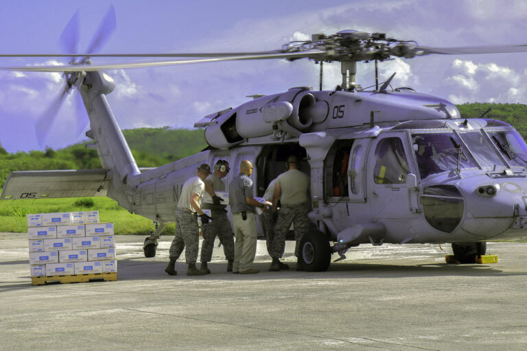 Five soldiers load boxes of water into a U.S. Navy helicopter on a tarmac