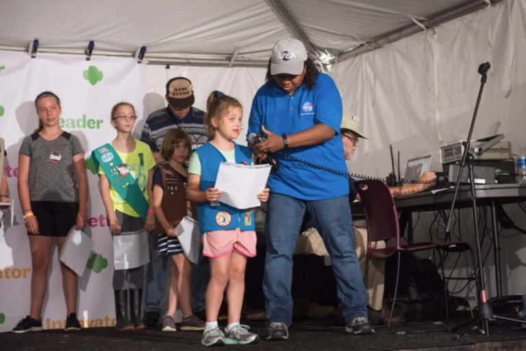 woman holding a microphone for a young girl with other girls in the background