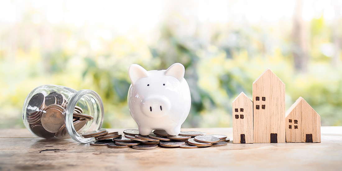 A piggy bank sitting on top of quarters that spilled from a glass jar next to small wooden houses