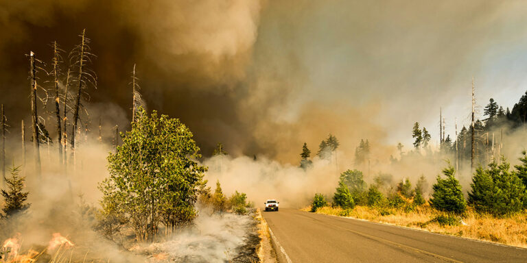 truck on road with wildfire behind smoke