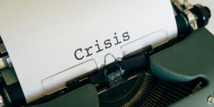 Green typewriter with white paper with only the word "Crisis" on it