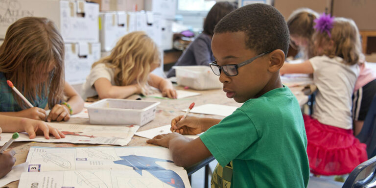 two young children at desk writing with pencil in right hand
