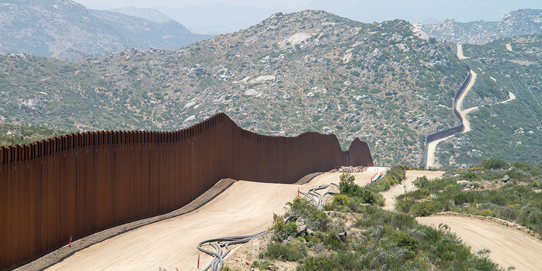mexican border, fence on left with woodsy mountain ahead