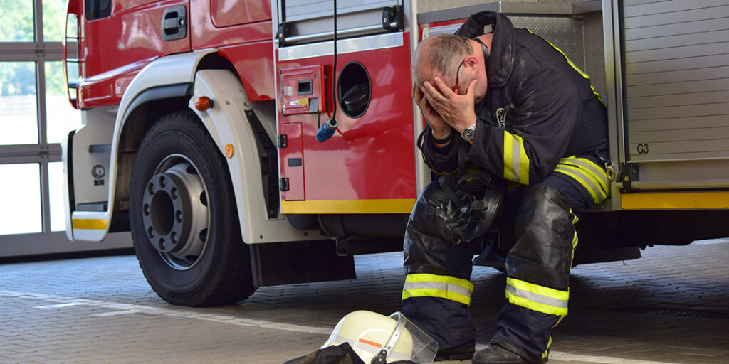 Firefighter appearing distressed sitting on side of fire truck.