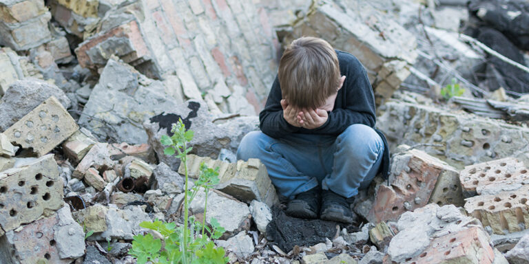 Sad, little boy near destroyed house.
