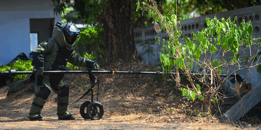 EOD officer in the explosive ordnance disposal suit using remote robot hand to check the unclear box beside the wall