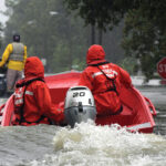 Coast Guardsmen in an inflatable motor boat motoring down a flooded street