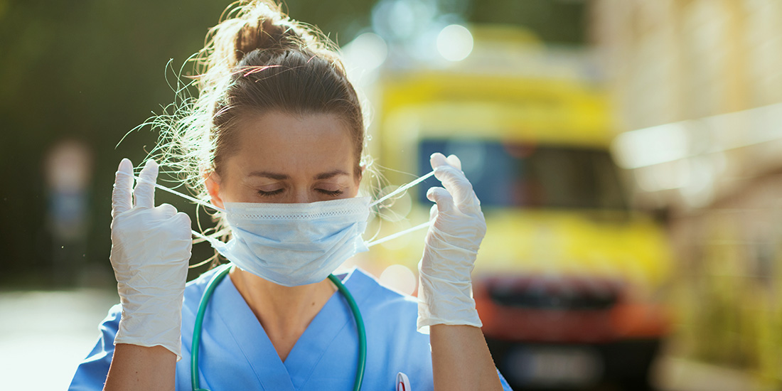 coronavirus pandemic. modern paramedic woman in scrubs with stethoscope and medical mask outside near ambulance.