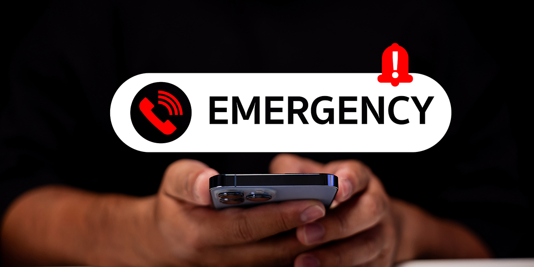 A person holds a smartphone in both hands against a dark background. Above the phone, a large notification-style banner displays a red phone icon, the word “EMERGENCY” in bold black letters, and a red alert symbol. The image illustrates an emergency alert, urgent communication, or mobile emergency notification system.